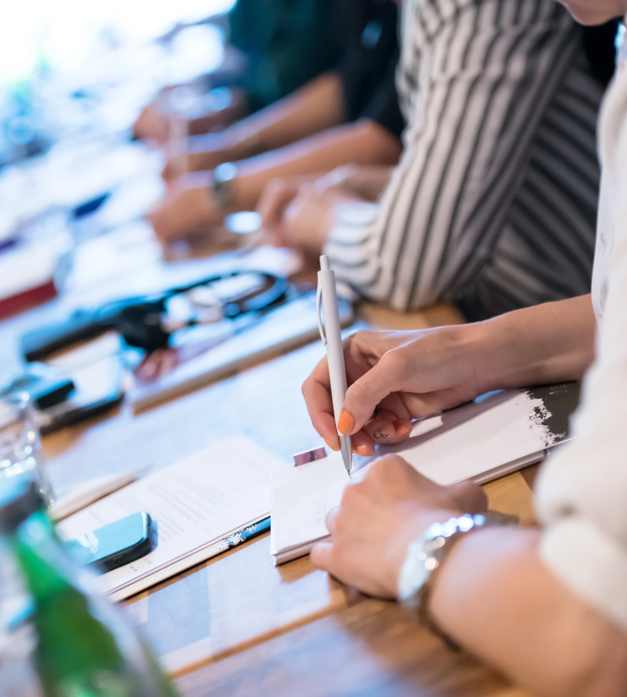 Das Bild zeigt eine Reihe an Menschen, die an einem Tisch sitzt und sich Notizen zu Prozessoptimierung und LEAN-Management macht